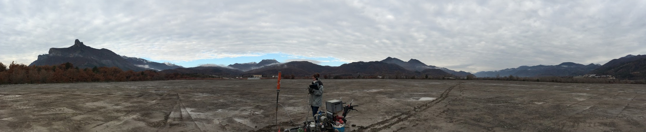 Panorama einer Fläche mit Sondiergerät, einer Person, und Bergen im Hintergrund